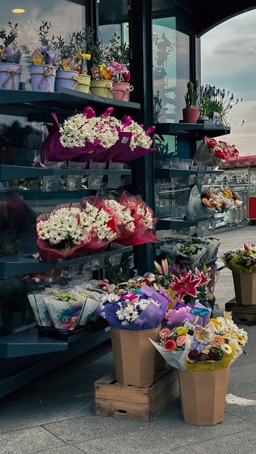 An indoor display of various floral arrangements including bouquet and potted plants at Swiss Cottage station, arranged on dark grey shelves and in containers. The bouquets feature a mix of fresh flow